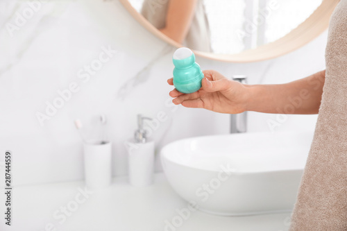 Young woman with roll on deodorant in bathroom  closeup view. Space for text