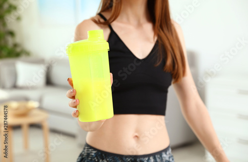 Young woman with bottle of protein shake at home, closeup view