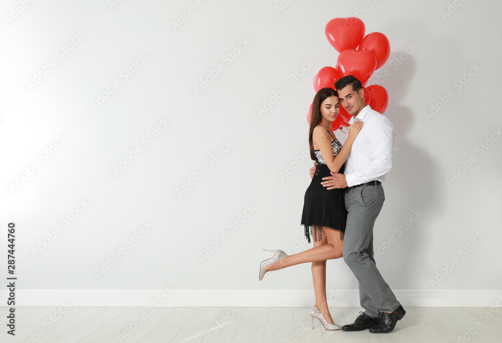 Beautiful couple with heart shaped balloons near light wall, space for text