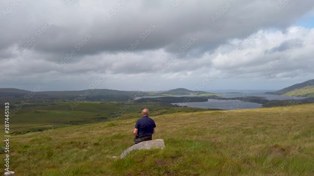 Old man sitting on boulder overlooking Irish spectacular countryside sights of into distance. Old man sitting on boulder overlooking Irish spectacular countryside sights of into distance.