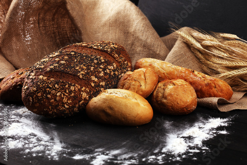 Assortment of baked bread and bread rolls on black table background