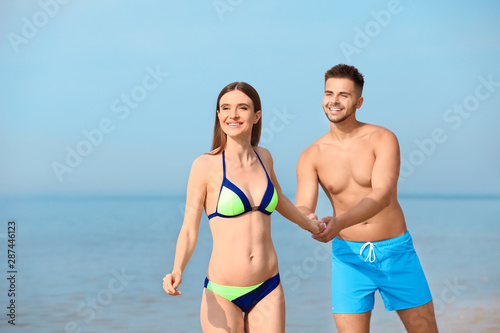 Young woman in bikini with her boyfriend on beach, space for text. Lovely couple