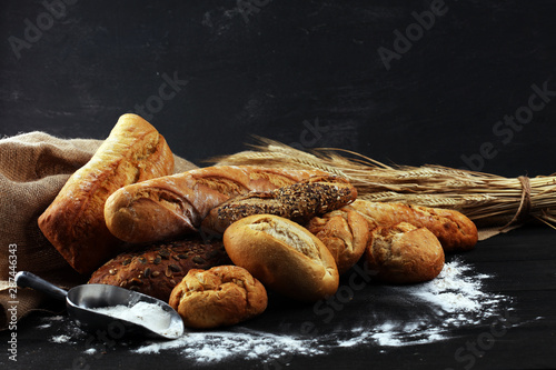 Assortment of baked bread and bread rolls on black table background
