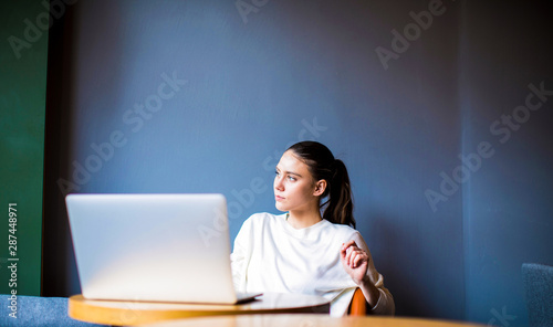Thoughtful business woman thinking about new financial ideas, sitting with laptop computer in coffee shop. Pensive female professional writer dreaming about something during work on portable netbook
