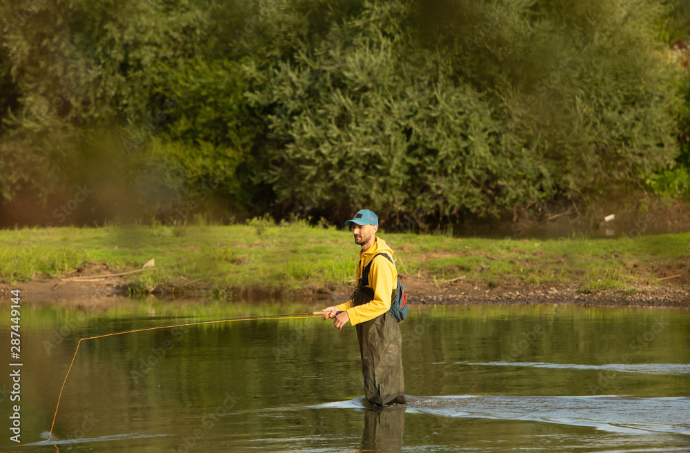 The fisherman stands at waist-deep in water. A man in a special waterproof suit throws a fishing rod The fisherman stands at waist-deep in water. A man in a special waterproof suit throws a fishing rod
