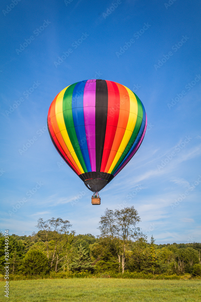 Fototapeta premium Rainbow colorful hot-air balloon floats on a summer morning with bright blue sky 