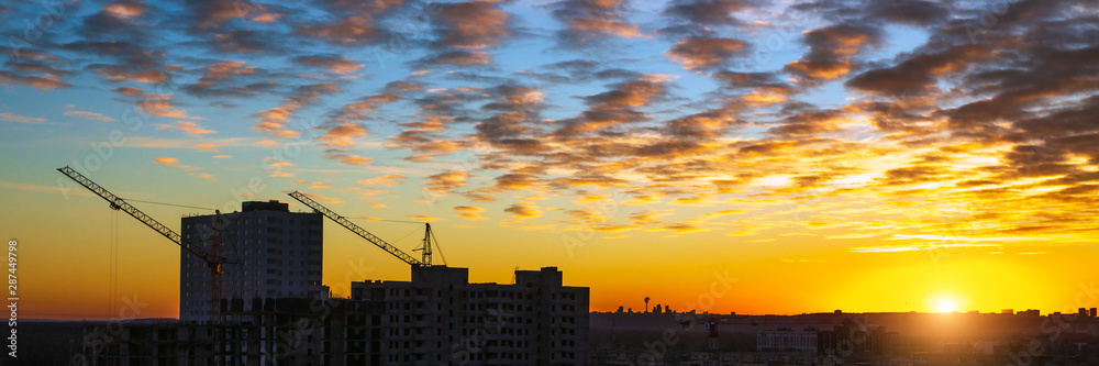 Urbanscape with sunset, cirrus clouds, building under construction and cranes. Concept for banner page wallpaper design