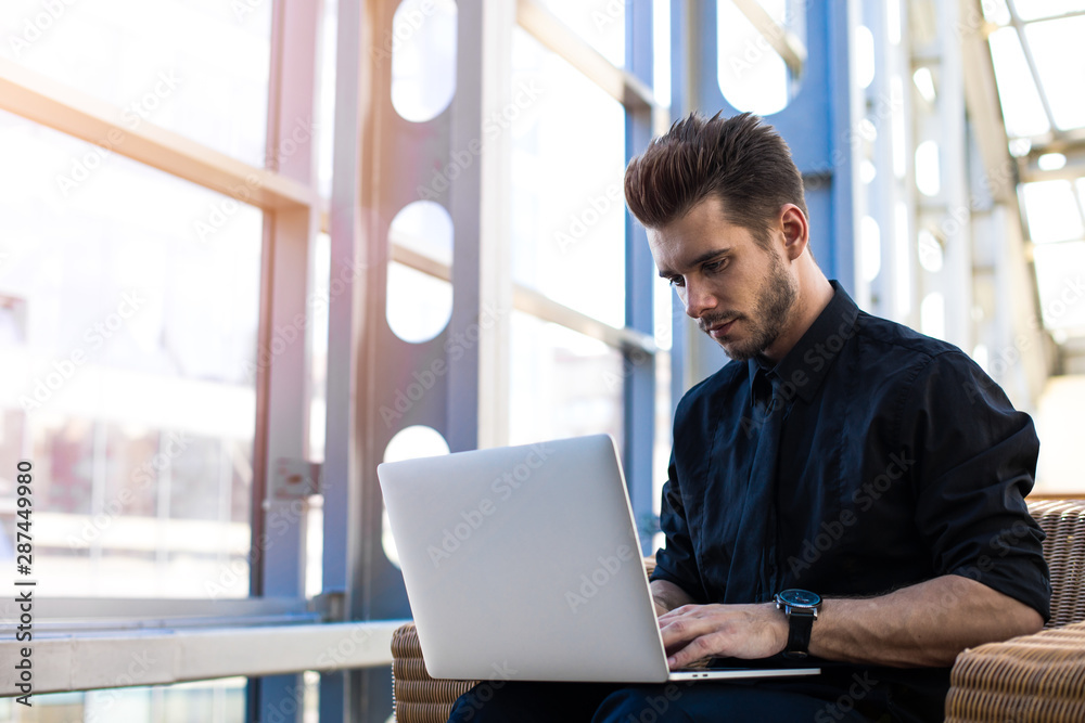 Man skilled entrepreneur checking e-mail on laptop computer while waiting plane in airport terminal sitting near window with copy space for promotional text. Economist online booking via notebook