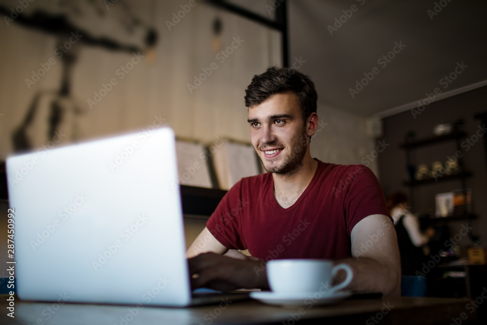 Happy smiling hipster guy having video conference via laptop computer while sitting in coffee shop. Joyful handsome male having online call via netbook during recreation time in restaurant. Happy smiling hipster guy having video conference via laptop computer while sitting in coffee shop. Joyful handsome male having online call via netbook during recreation time in restaurant.