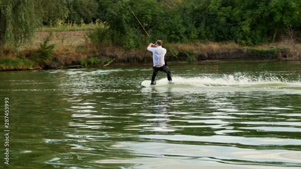 Extreme businessman in a suit with a tie and sunglasses rides on wakeboard and jumping on a springboard on a lake at sunset Extreme businessman in a suit with a tie and sunglasses rides on wakeboard and jumping on a springboard on a lake at sunset