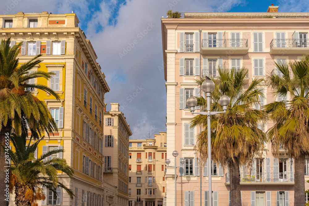 Nice, France, colorful facade, with typical windows and shutters, in a charming street with palm trees 