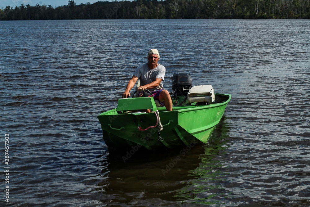 Older gray haired man in his bright green fishing boat enjoying a sunny summer weekend on the Mattaponi River in Virginia United States