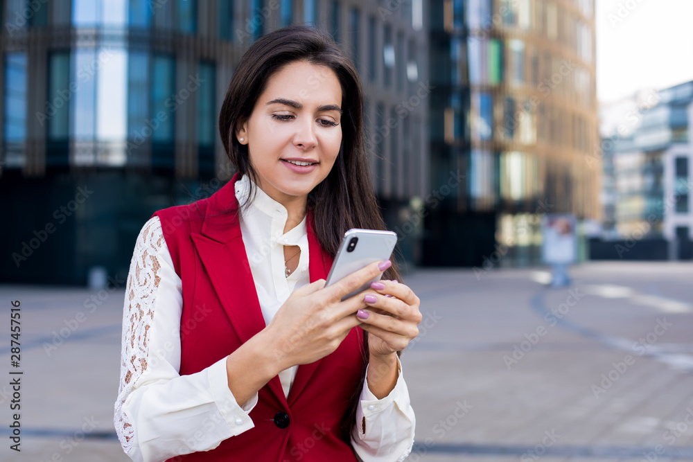 Happy smiling woman professional government worker reading good news in messenger on mobile phone while standing outside contemporary office building with copy space. Cheerful female chatting Happy smiling woman professional government worker reading good news in messenger on mobile phone while standing outside contemporary office building with copy space. Cheerful female chatting