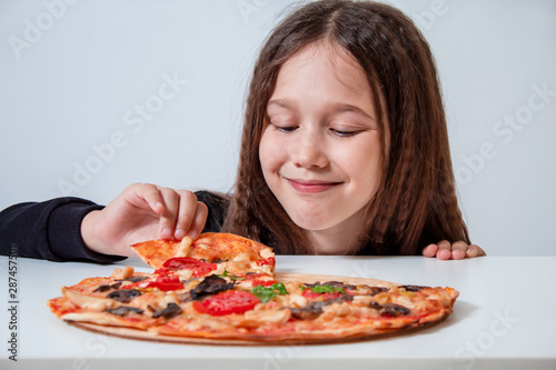 The little girl takes a slice of pizza. The child eats pizza