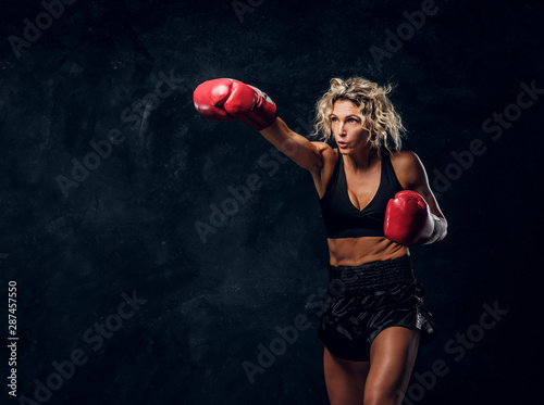 Sportive muscular woman is demonstrating her boxing exercises, wearing gloves. © Fxquadro