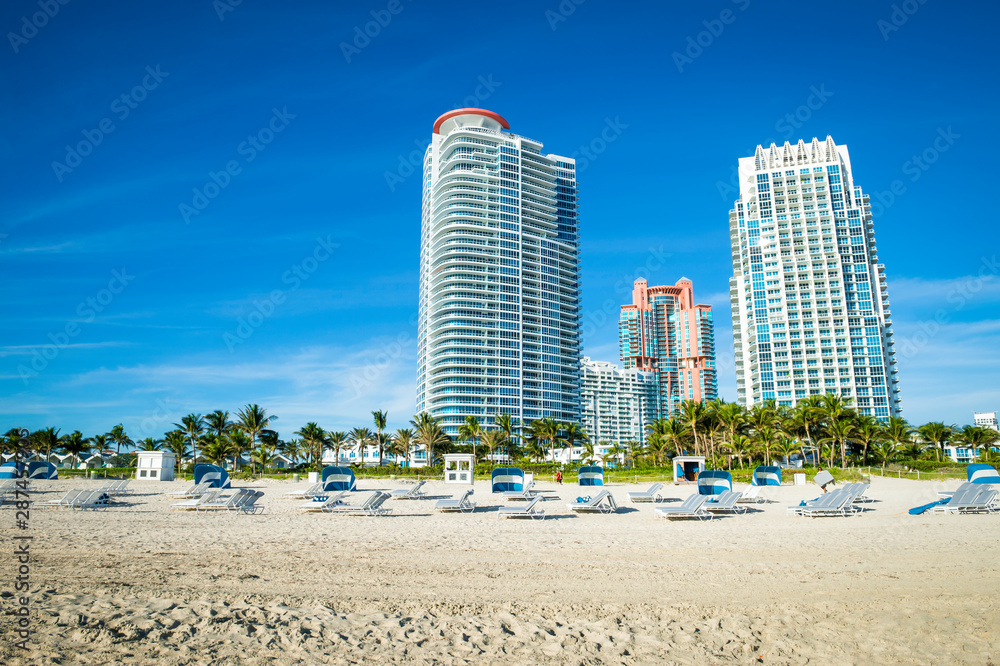 Bright scenic morning view of the Miami skyline with lounge chairs waiting for sunbathers on the shore of South Beach at South Pointe Bright scenic morning view of the Miami skyline with lounge chairs waiting for sunbathers on the shore of South Beach at South Pointe