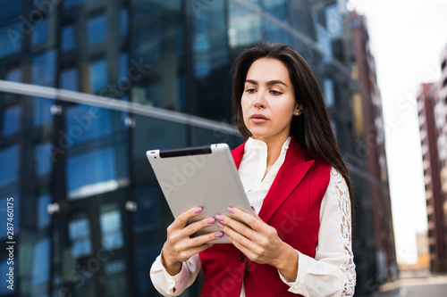 Female professional financier checking e-mail on portable touch pad while standing outside company. Female entrepreneur using digital tablet for char, standing near business centre during break at job