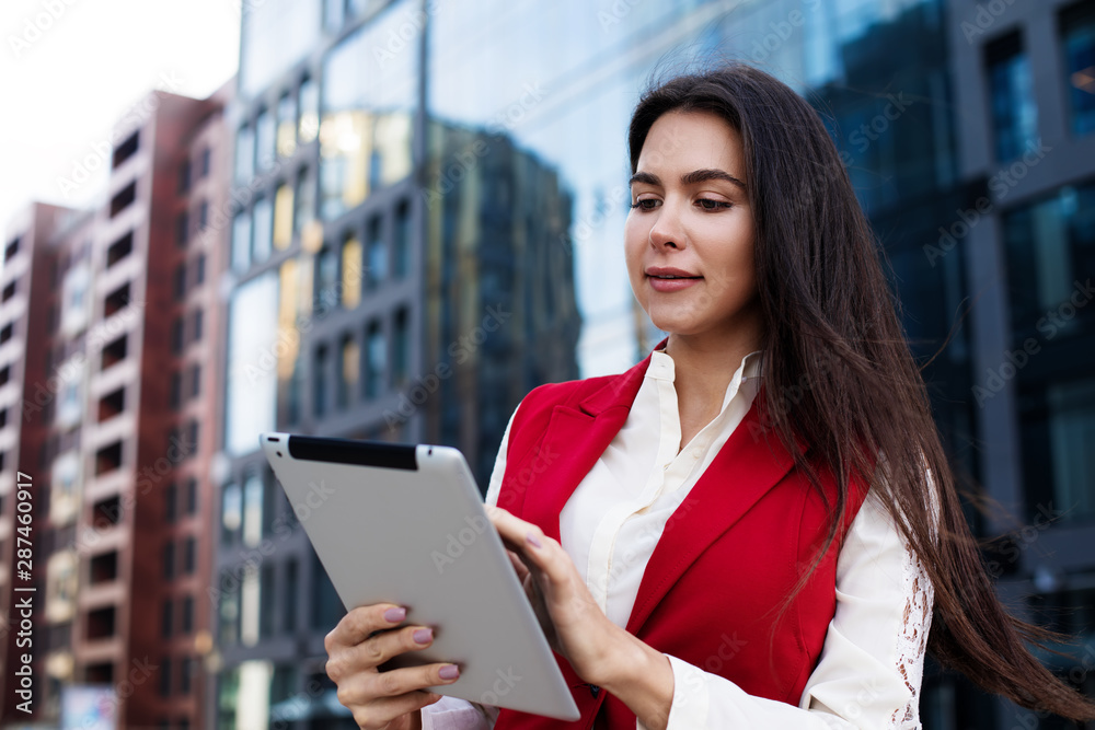 Young woman intelligent secretary searching information on modern touch pad while standing outdoors against modern business building. Female successful boss using apps on digital tablet Young woman intelligent secretary searching information on modern touch pad while standing outdoors against modern business building. Female successful boss using apps on digital tablet
