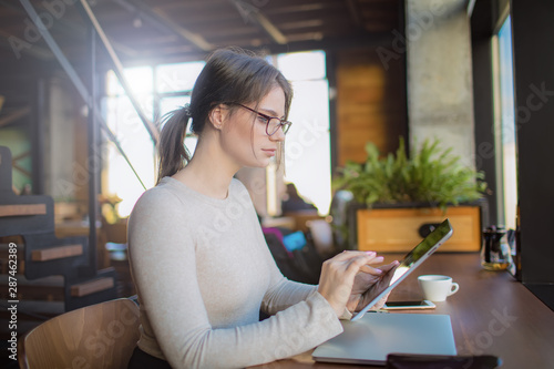 Smart woman skilled marketing specialist publication information on web site via portable touch pad computer while sitting in co-working coffee shop. Female online banking via digital gadget