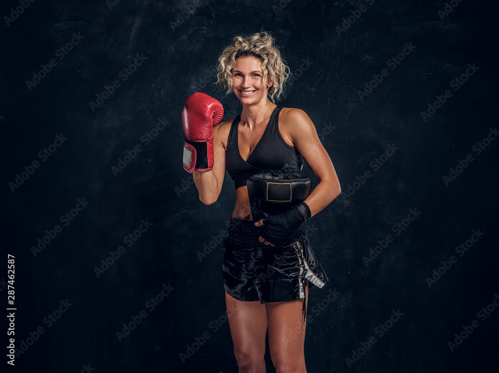 Happy smiling female boxer is posing for photographer at dark photo studio. Happy smiling female boxer is posing for photographer at dark photo studio.