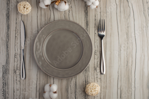 Empty gray dish with knife and fork on a slate background with a cotton branch, with copy space for your menu or recipe. Menu card for restaurants and table setting. Horizontal photo. Flat lay