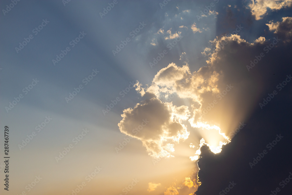 sky in shades of blue and yellow illuminated by sun rays clouded by clouds