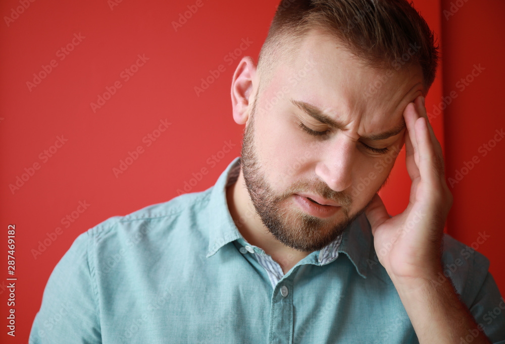 Fototapeta premium Young man suffering from headache on color background