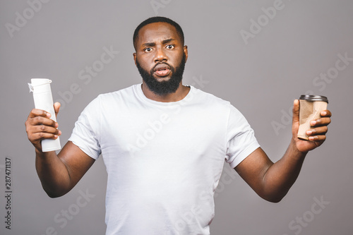 Zero waste concept. Young african american man making choose between cup of coffee and recycle one standing over isolated grey background.