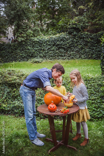 Happy halloween. Father and two daughter carving pumpkin for Halloween outside and pulls seeds and fibrous material from a pumpkin before carving for Halloween. Happy family © Evgeniya Biriukova