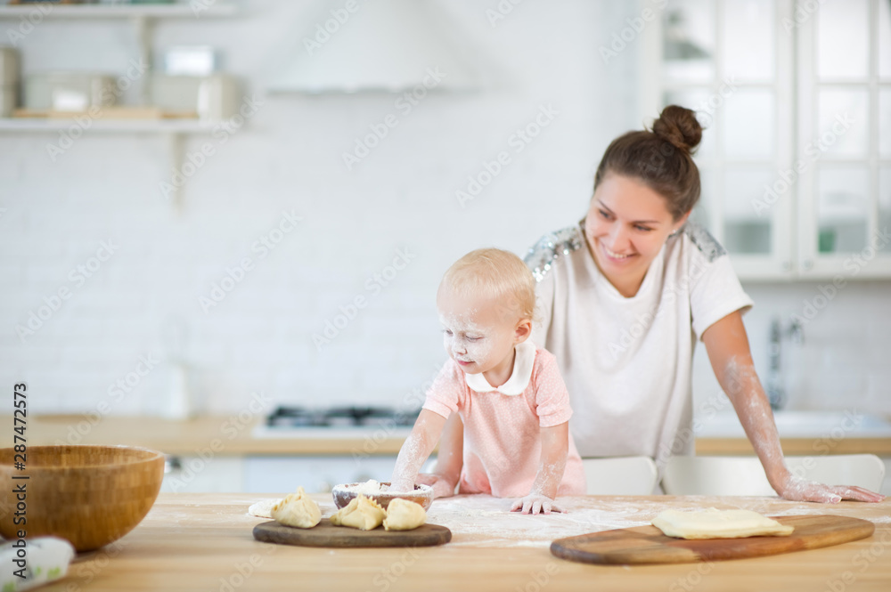 Fototapeta premium mom looks at her little daughter playing in the kitchen with flour