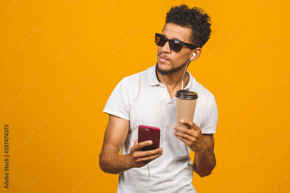 Smiling black young man in glasses holding phone isolated on yellow studio background with copy space aside, african guy using mobile applications, texting. Smiling black young man in glasses holding phone isolated on yellow studio background with copy space aside, african guy using mobile applications, texting.