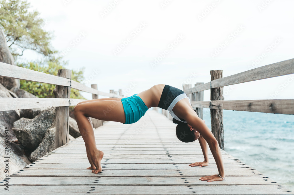 Young woman doing yoga on the wooden bridge