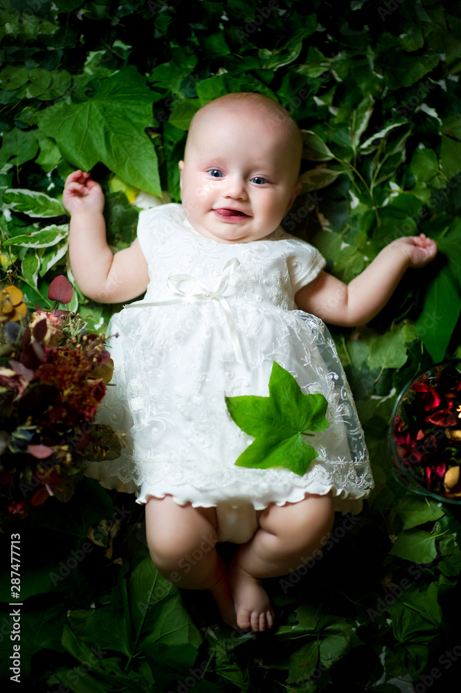 little girl in a white dress lies on green leaves. Vertical photo.
