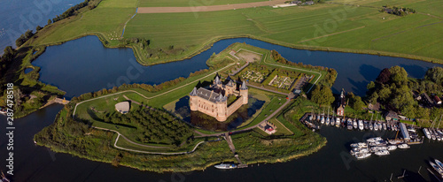 Aerial panoramic view of the island with the Muiderslot castle in Muiden near Amsterdam and its lush gardens at the IJsselmeer with surrounding water entrenchment at sunset
