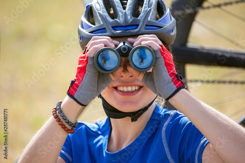 Beautiful girl cyclist looks through binoculars.