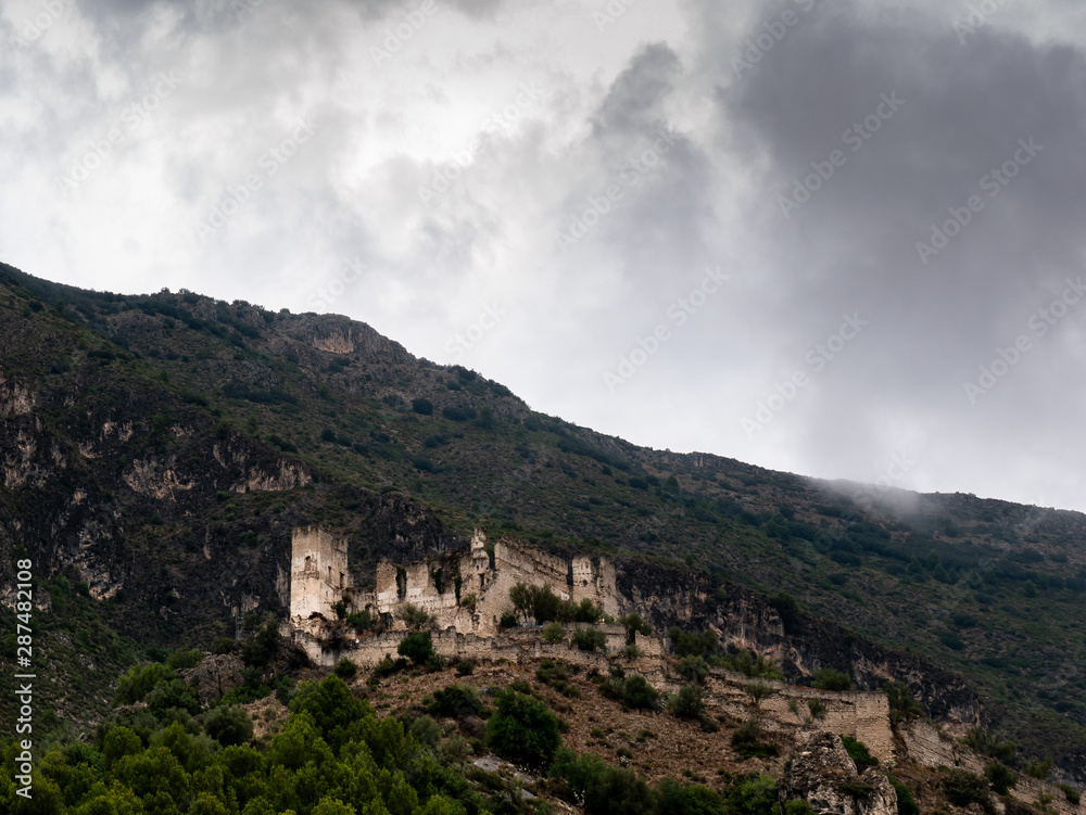 castillo templario en ruinas en lo alto de una colina rodeado de montañas con cielo nublado 