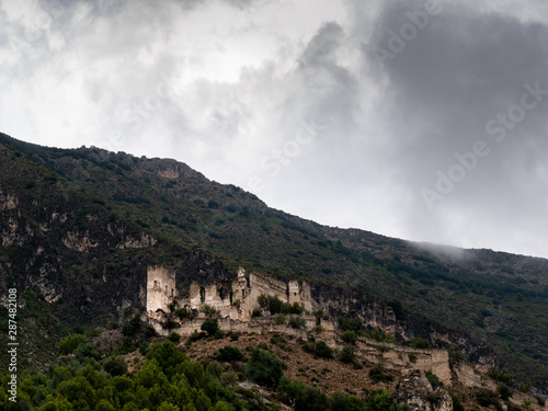castillo templario en ruinas en lo alto de una colina rodeado de montañas con cielo nublado 