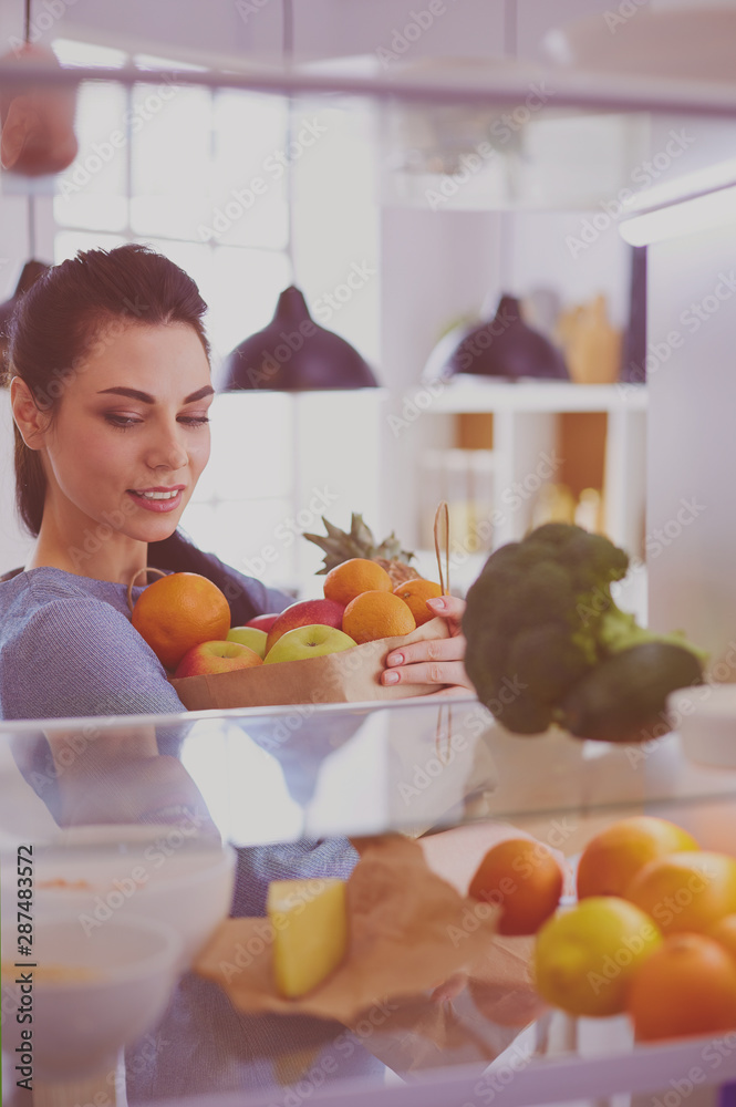 Smiling woman taking a fresh fruit out of the fridge, healthy food concept Smiling woman taking a fresh fruit out of the fridge, healthy food concept