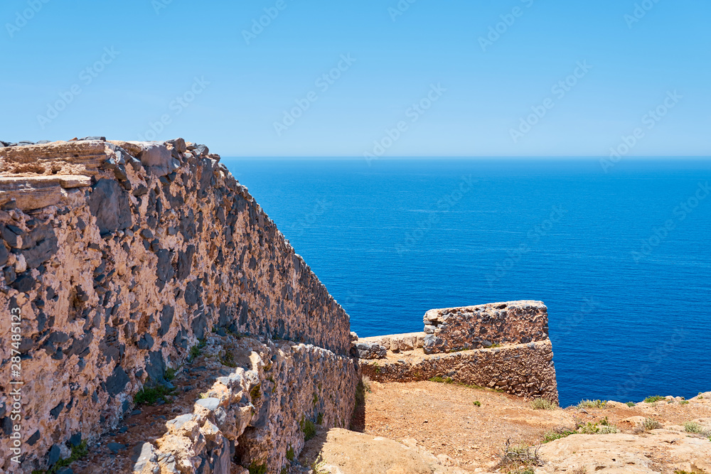                                Ruins of old historical wall with blue sea and horizon on a background in Crete, Greece. Copy space. 