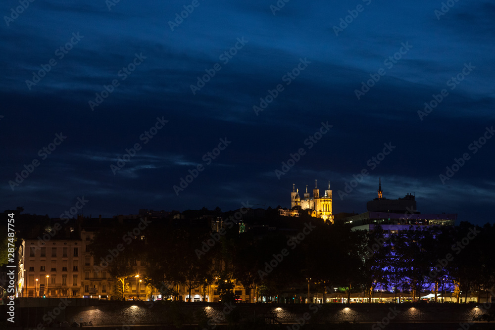 Panorama of Colline de Fourviere Hill at night seen from the riverban of the Rhone river. Notre Dame de Fourviere, the main basilica church of the city, is visible