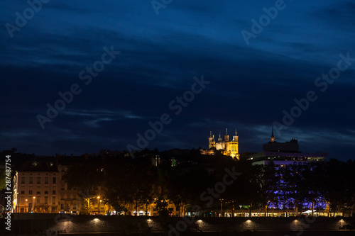 Panorama of Colline de Fourviere Hill at night seen from the riverban of the Rhone river. Notre Dame de Fourviere, the main basilica church of the city, is visible