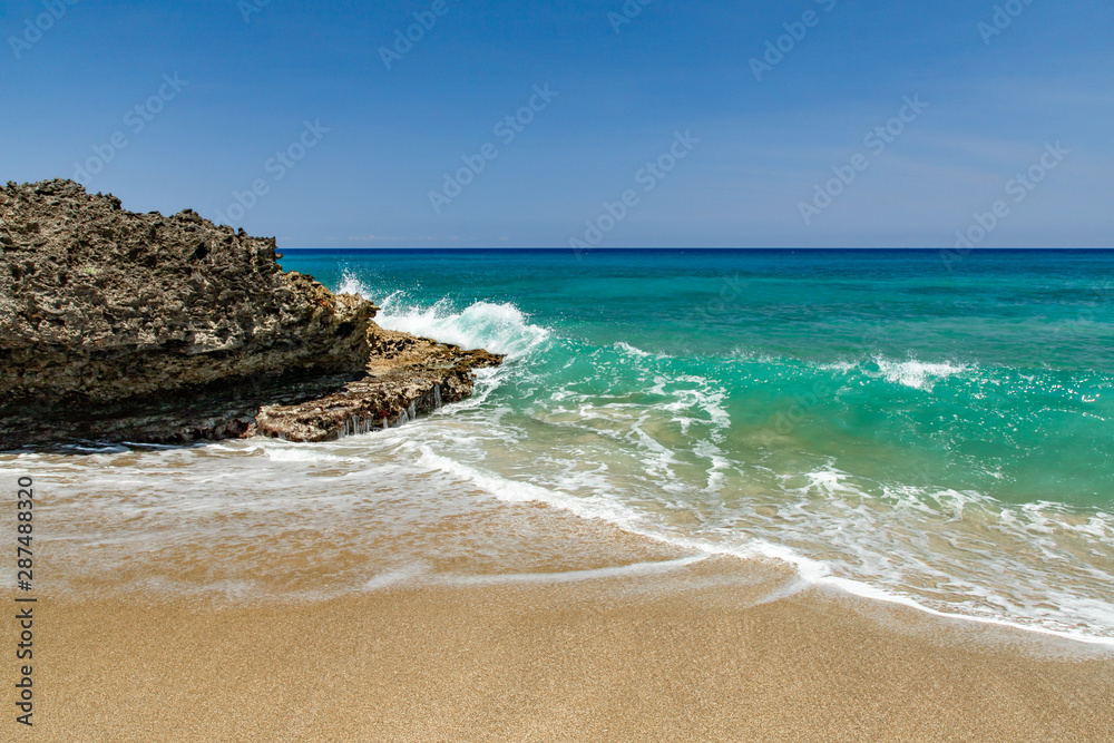 Ocean foamy waves at the beach near rocks, crystal clear turquoise water, Sosua, Puerto Plata, Dominican Republic