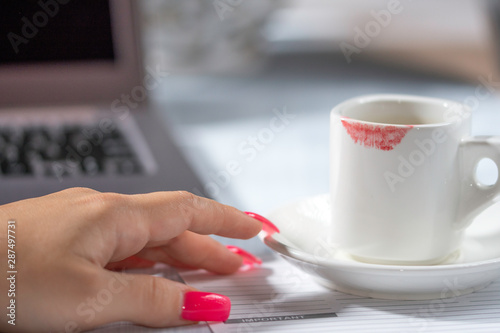 Female hand with cup of coffee, office desk, office coffee break