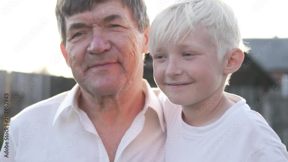 Close-up of grandfather with grandson at daughter on sunset background. The boy kisses his cute old grandfather and smiles. Close-up of grandfather with grandson at daughter on sunset background. The boy kisses his cute old grandfather and smiles.