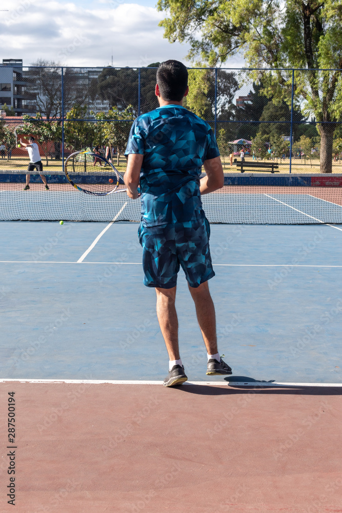 Hombre adulto latino con barba de camiseta azul en pantaloneta jugando  tenis con amigo en cancha profesional hispano Stock Photo | Adobe Stock