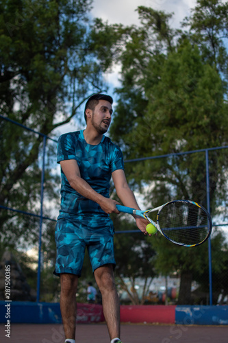 Hombre adulto latino con barba de camiseta azul en pantaloneta jugando tenis  con amigo en cancha profesional  hispano © Andres Saa