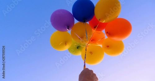 A large bunch of yellow Helium ballons straining on their strings against a sunny sky with white clouds, A lot of flying balloons with helium in blue sky with clouds.