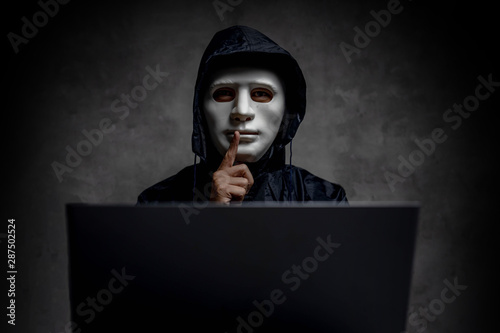 Hacker wearing a white mask in front of his computer. hacker hacks network, Space for text. photo