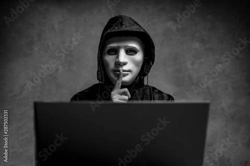 Canvas Print Male hacker hidden face with the mask accessing to personal information on laptop in the dark