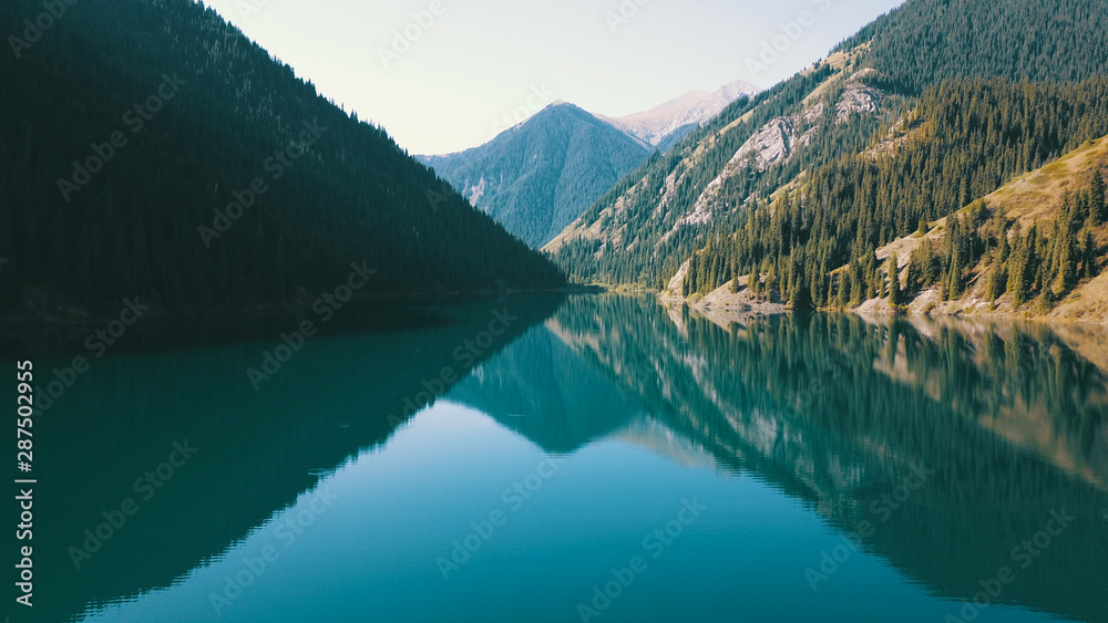 Fototapeta premium Kolsay lake located in the mountains of Kazakhstan. Turquoise water as a mirror. The water reflects the mountains, green hills, tall spruce, grass, sky and clouds. Beautiful landscape of mountain lake